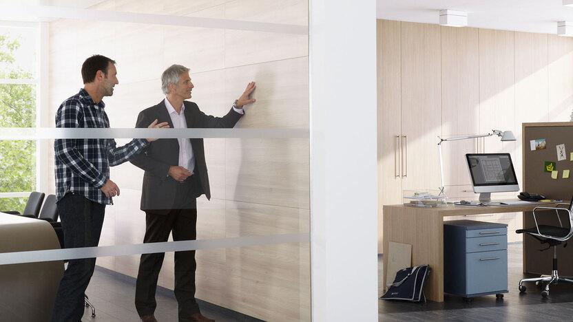 Impression eines Büros mit abgeschlossenem Raum mit Glaswand und offener Bürogestaltung.